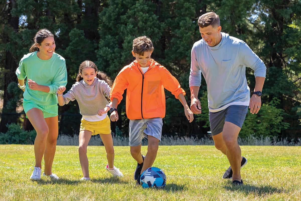 Pappa och mamma spelar fotboll med sina barn, alla bär smartwatches anpassade för barn.