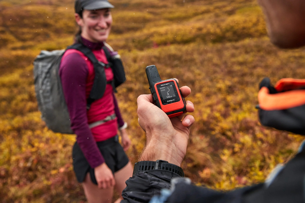 Bilden visar två vandrare i vildmarken, med fokus på en hand som håller en Garmin inReach Mini.
