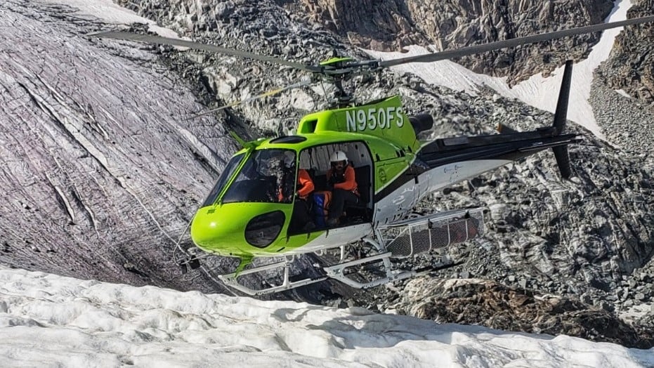Grön räddningshelikopter hovrar över glaciär under räddningsinsats i Wyoming