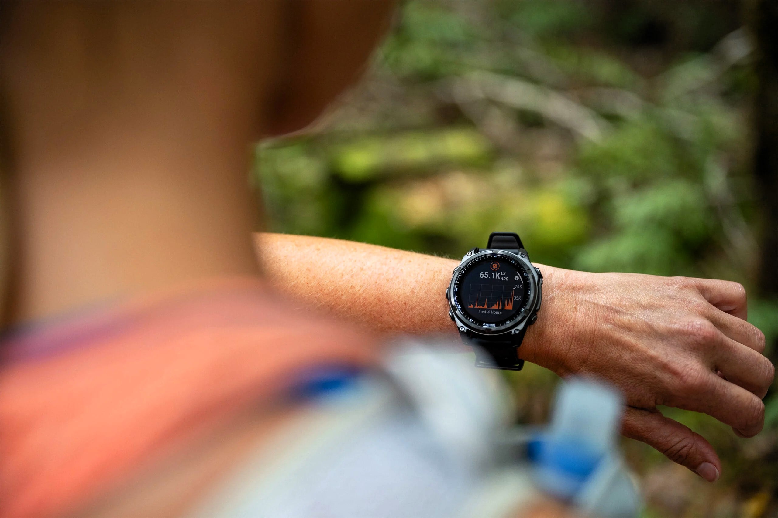 Person utomhus som tittar på en Garmin-smartwatch med aktivitetsdata på skärmen, i en skogsmiljö.