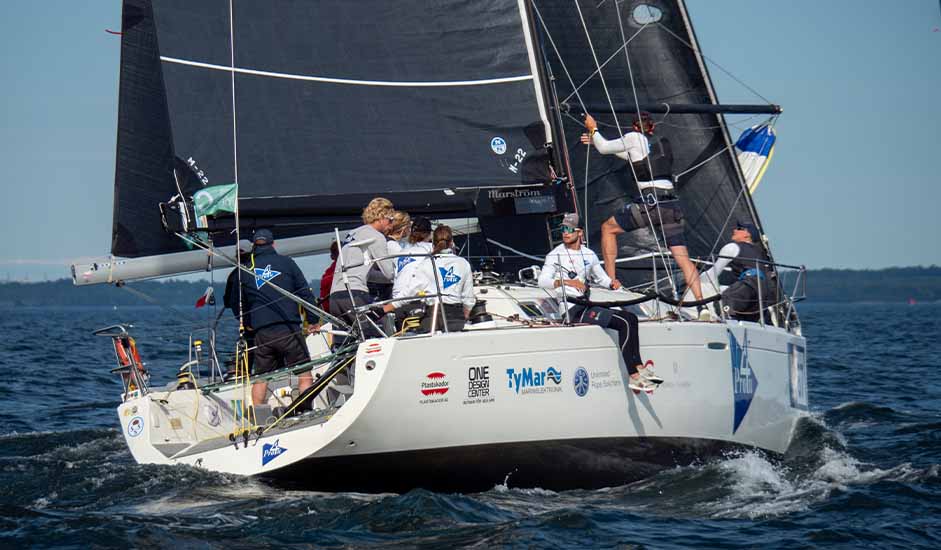 Pro4U-teamet kappseglar med svart storsegel, besättningen arbetar aktivt ombord under race.