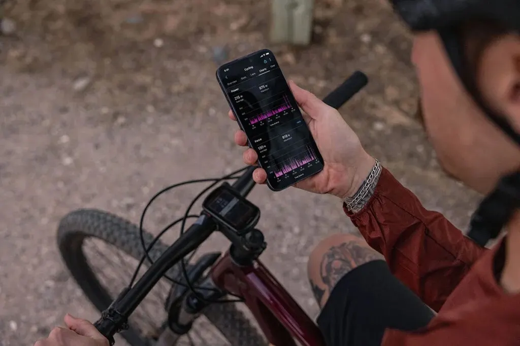 Cyklist visar effektdata i mobilen ovanför styret på en mountainbike