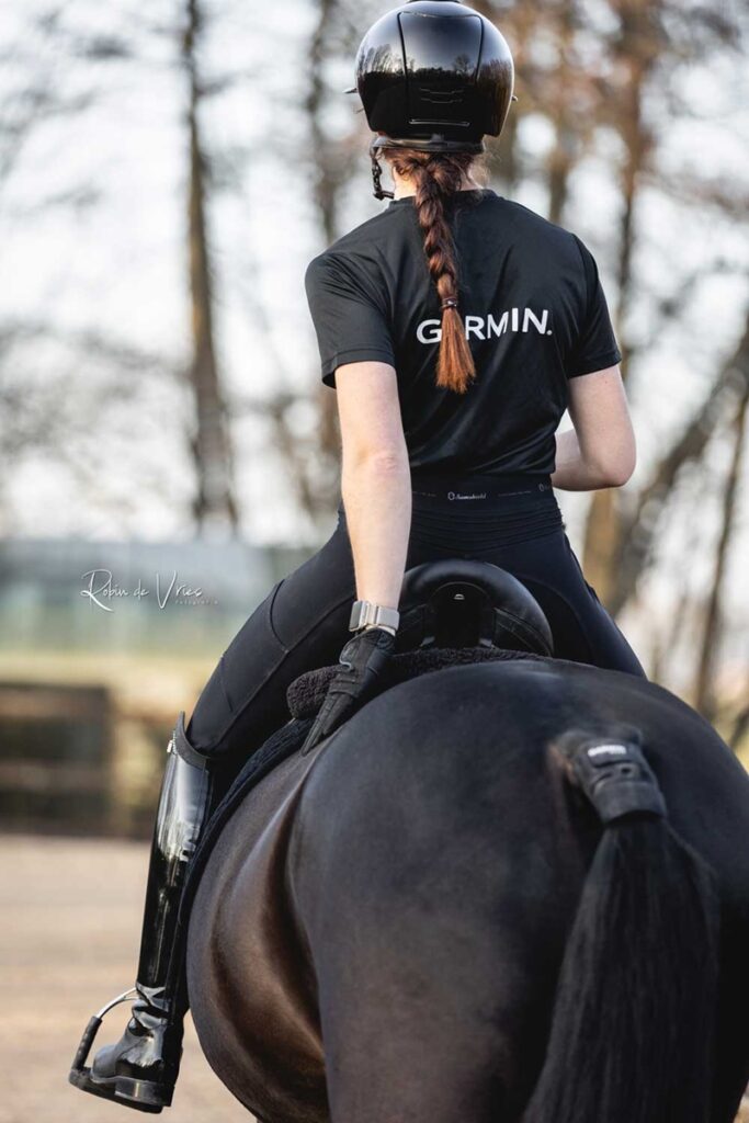 Dressyrryttare bakifrån på svart häst med Garmin Blaze fäst under svansroten