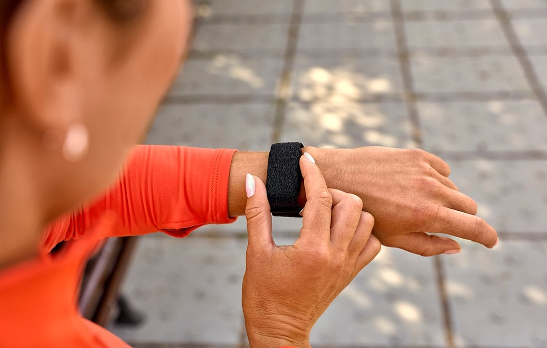 En person bär ett svart Garmin CIRQA Smart Band på handleden och justerar det med den andra handen utomhus.