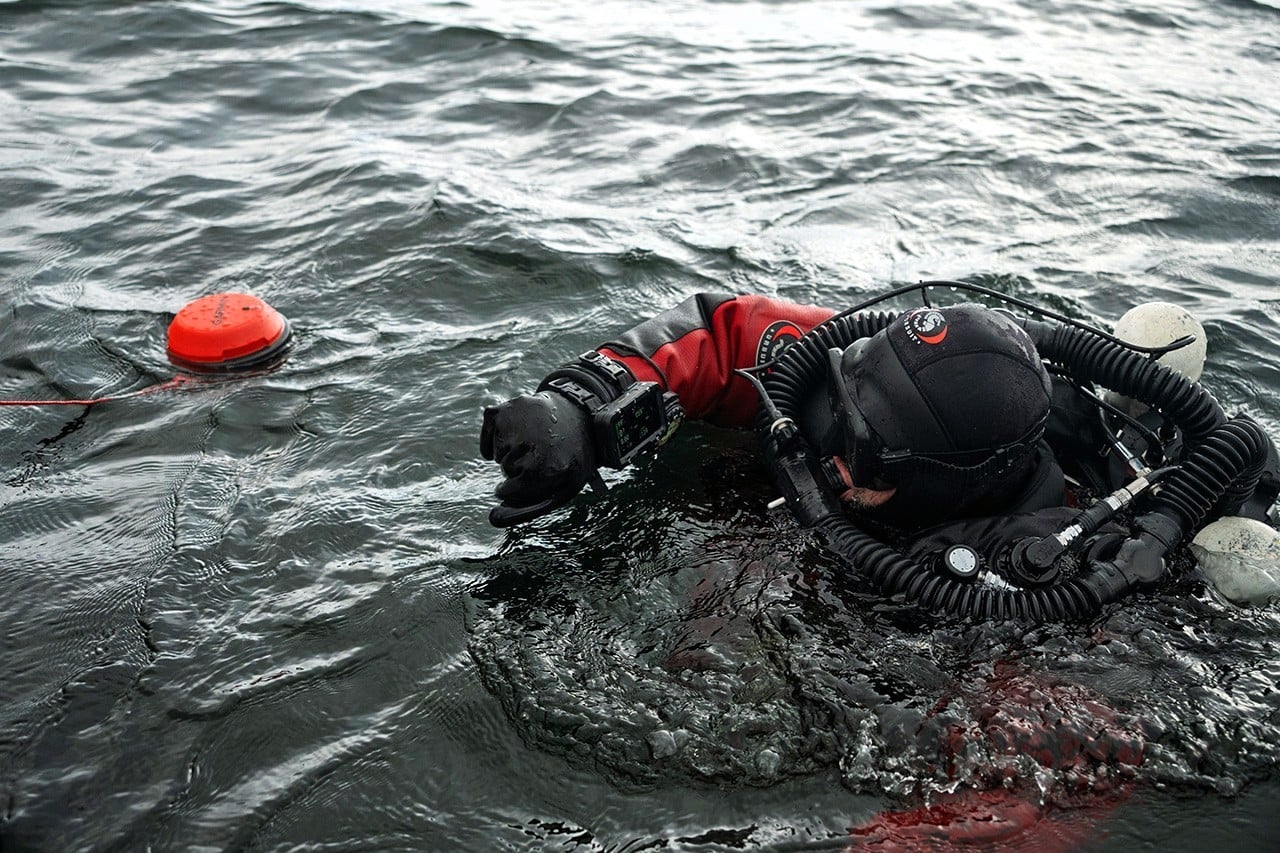 Dykare i röd torrdräkt vid ytan bredvid kommunikationsbojen Garmin Descent S1